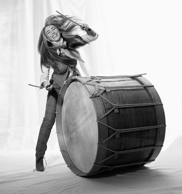Evelyn Glennie smiles, striking a large drum.