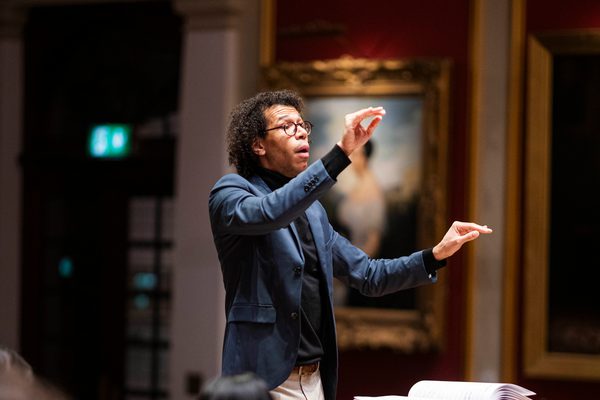 A conductor with student musicians on stage, mid-rehearsal.