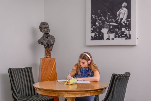 A student studies with headphones at a table, next to a bust of a musician.