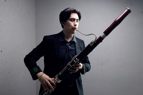 A bassoon player plays against a stark white background.