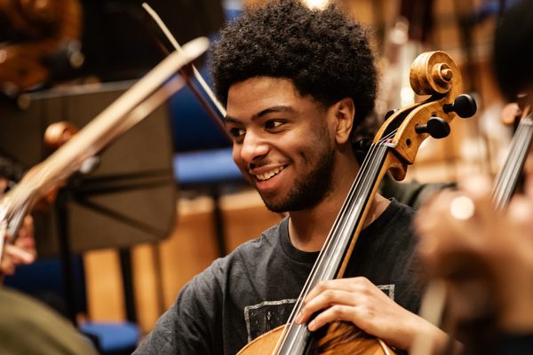 A cello students smiles in the middle of a busy ensemble.