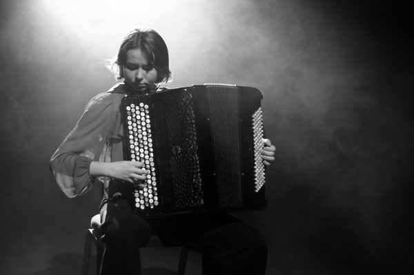 A close-up, black and white image of a hand playing the keys of an accordion.