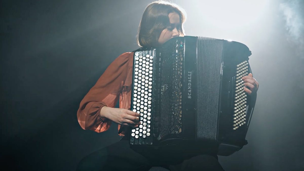 An accordion player in high contrast lighting performs solo on stage.