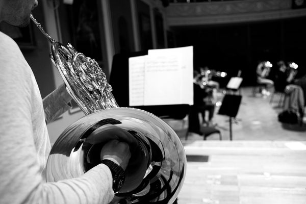 View over the shoulder of a horn player, looking out onto a music stand and empty auditorium (black and white).