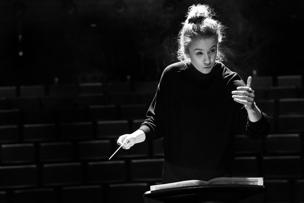 A conducting student in high contrast lighting stands at a podium.