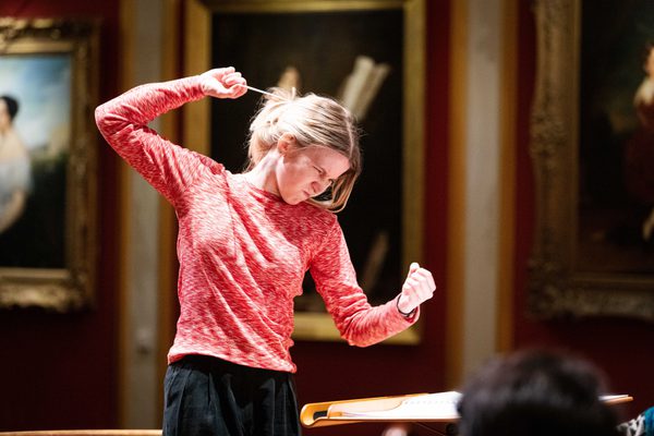 A conducting student raises a baton above shoulder height.