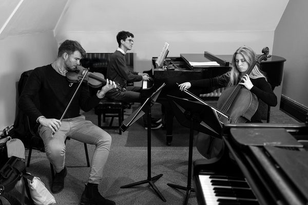 An ensemble piano tutor guides a piano accompanist in a practice room with a string duet (black and white).