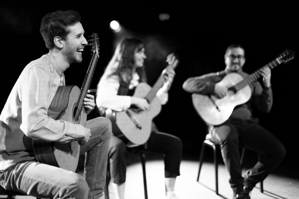 Three guitarists smile on stage in black and white.