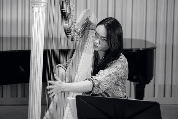 A Harp player plucks strings, glancing through the strings (black and white).