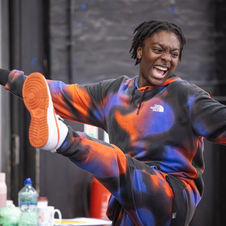 A young performer smiles, kicking their foot up in a dance move.