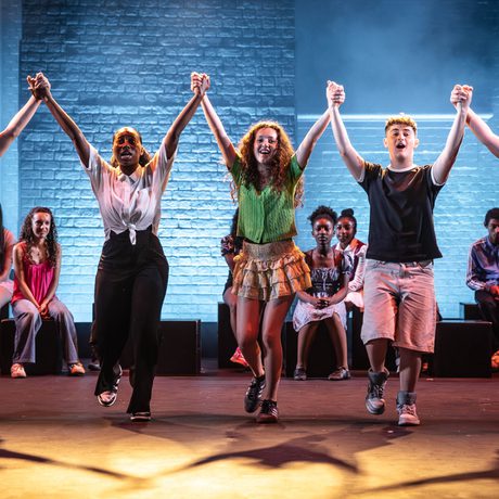 Four young performers stand in a row, holding hands high at the end of a performance.