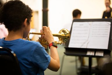 A young person plays a trumpet while reading sheet music.