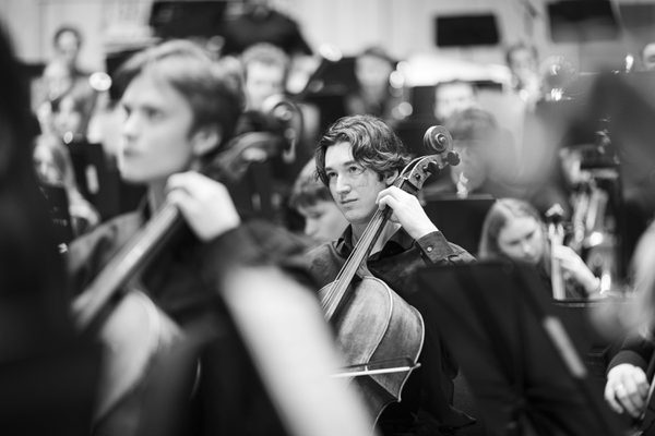 A cellist amidst a large ensemble.