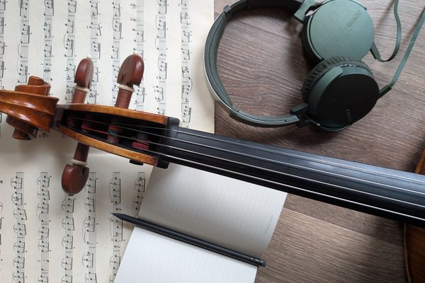 A close-up of the neck of a violin, with a manuscript, a notepad and some headphones.