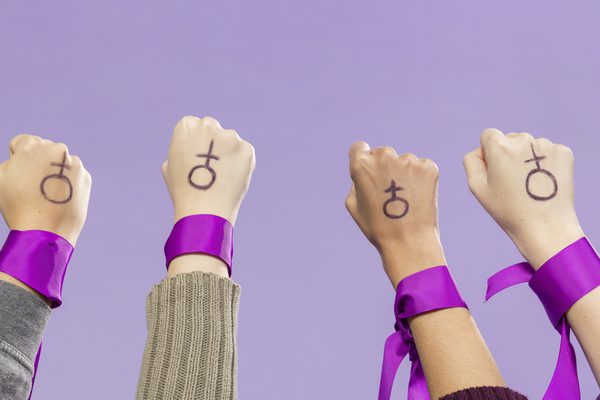 Four fists raised in the air with purple ribbons around the wrist, with the symbol for male drawn on the backs of their hands.