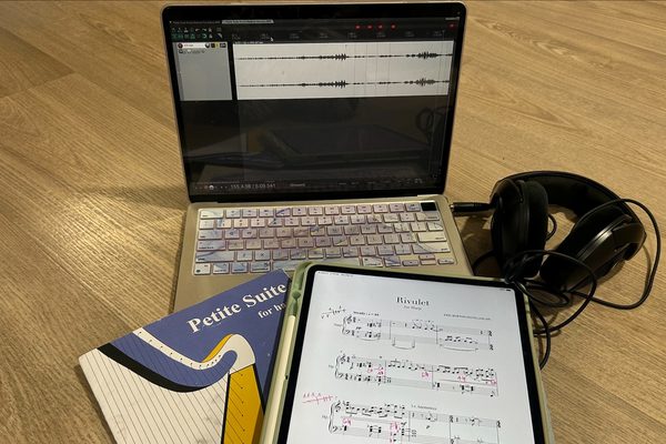 A manuscript, notepad and headphones sit on top of a laptop showing a digital recording.