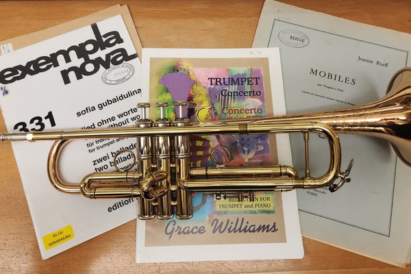 A trumpet lying on top of three musical manuscripts on a desk.