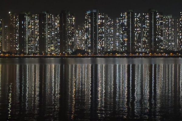 A city skyline at night, viewed across a large, reflective body of water.