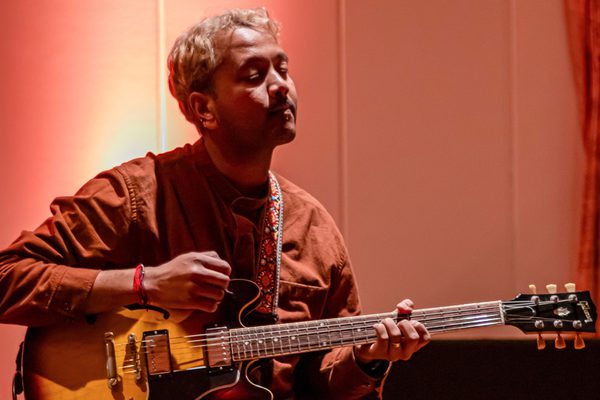 A guitarist mid-performance, bathed in red light.