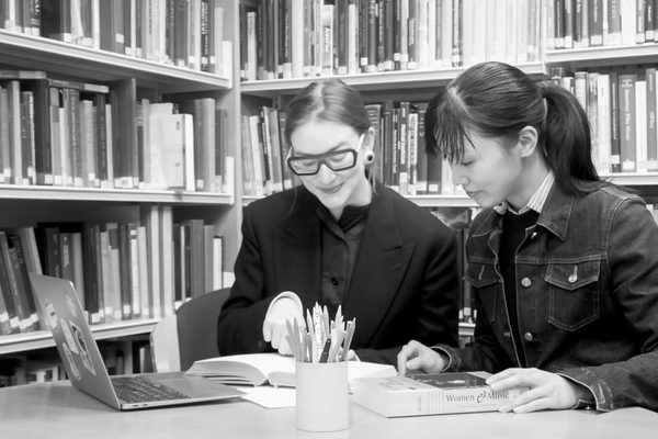 Two researchers study a book together in a library.