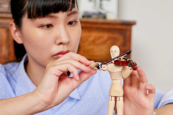 A woman holding a small wooden jointed model of a person playing a small model of a violin.