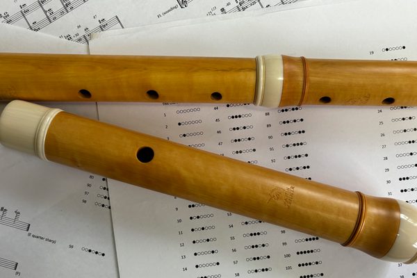 A light wood baroque flute lying on fingering charts and some music scores.