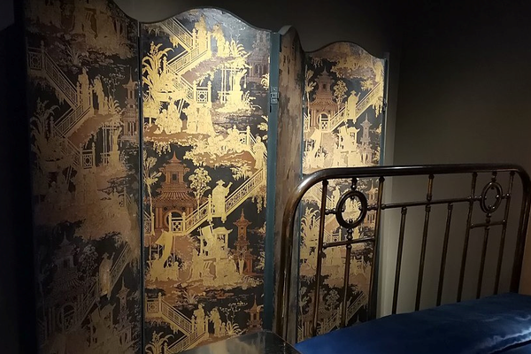 Marcel Proust’s black bed frame with a black and gold screen in the Musée Carnavalet, Paris.