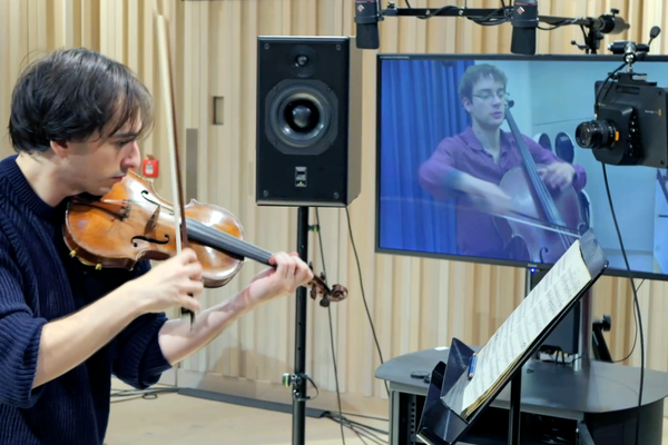 Violinist Basil Alter performs in the foreground, with cellist Constantin Siepermann on a screen, while 1300km apart from each other.