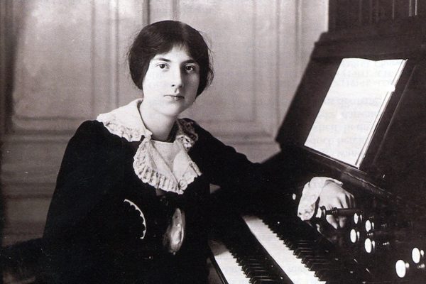 A woman sitting at a keyboard with her hair up, wearing a historical black dress with white cuffs and collar.