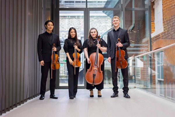 A string quartet hold instruments and smile to camera.