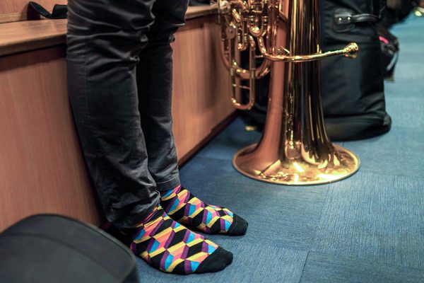 A person stands in their socks with a tuba on the ground alongside.