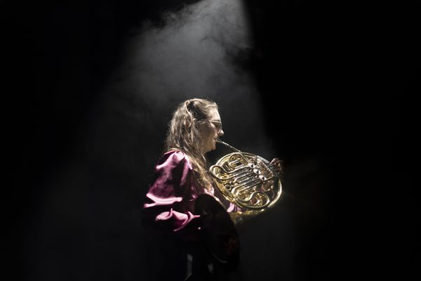 Profile of a horn player bathed in a spotlight.