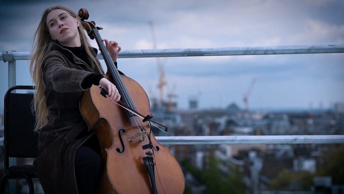 A cellist plays overlooking a busy urban backdrop.