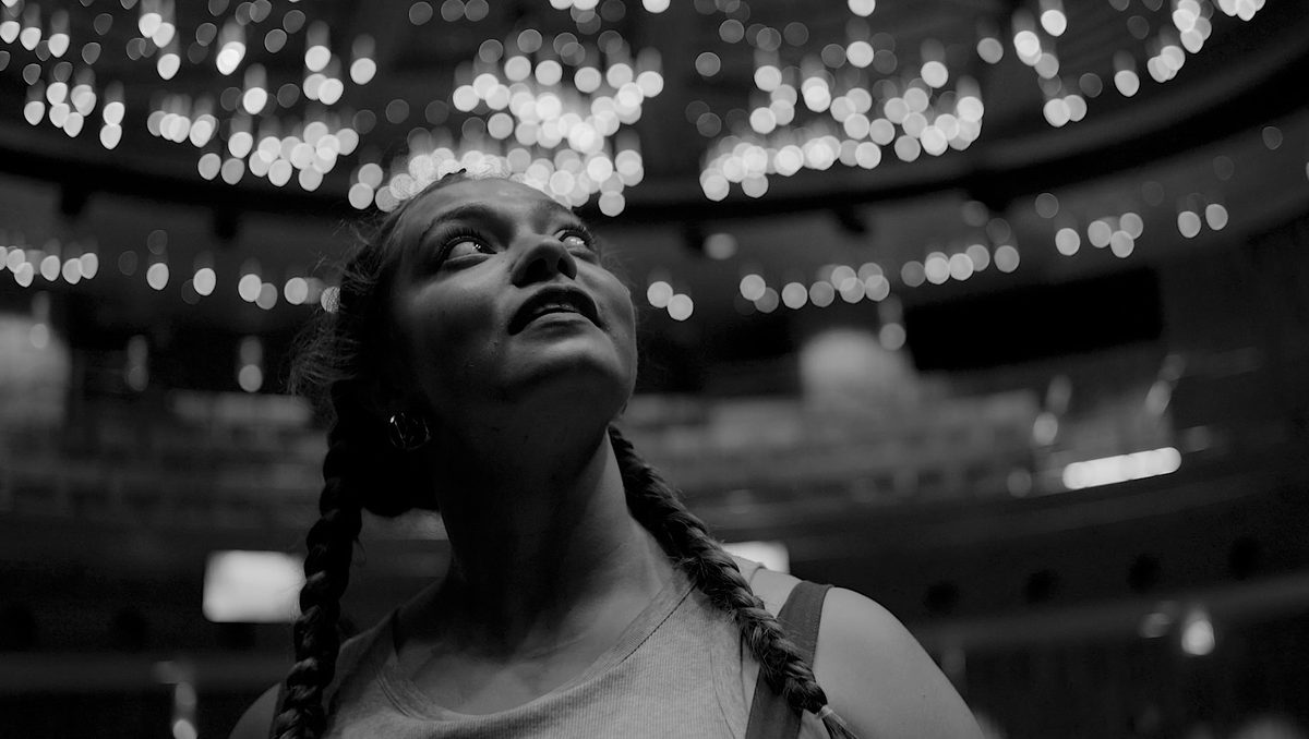 A student looks hopefully towards an auditorium ceiling of bright lights.