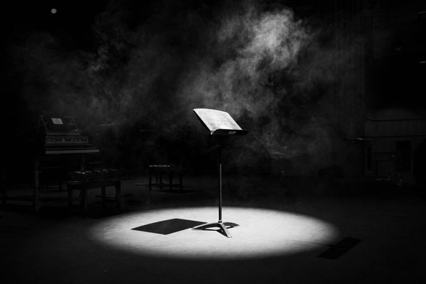 A music stand stands in the spotlight of an empty stage.