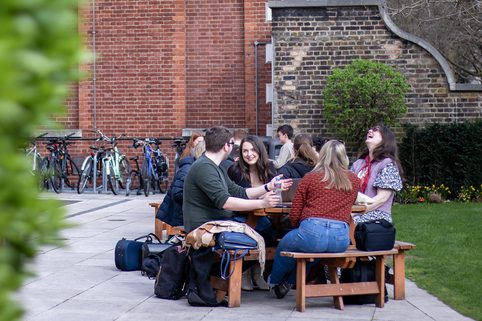 Students sit outside, chatting at a table.