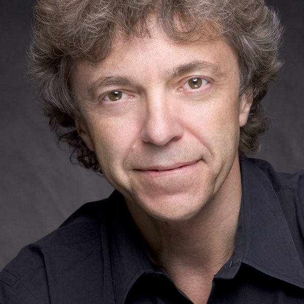A headshot of Pascal Roge smiling to camera with a dark backdrop