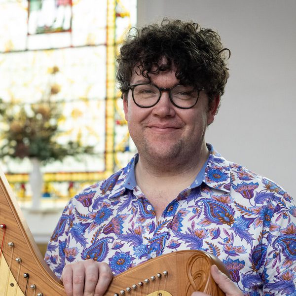 Alexander Rider smiels for camera, holding a harp.