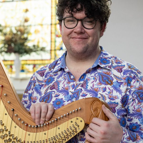 Alexander Rider smiels for camera, holding a harp.