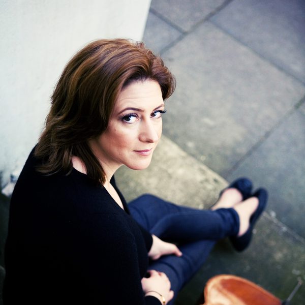 Ali Mackenzie sits outside with a cello leaned against a step.