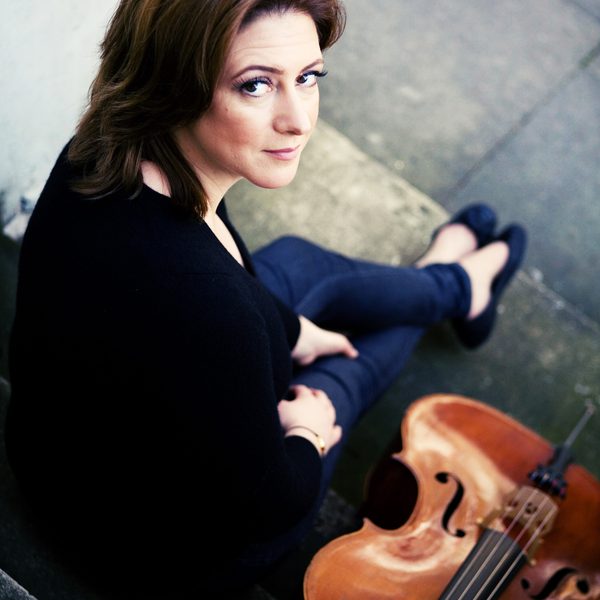 Ali Mackenzie sits outside with a cello leaned against a step