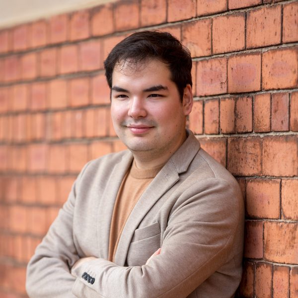 Alim Beisembayev leans against a brick wall, arms folded.