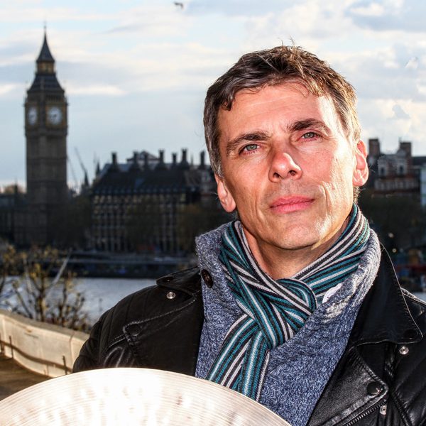 Andrew Barclay stands holding a cymbal with the Houses of Parliament in the background