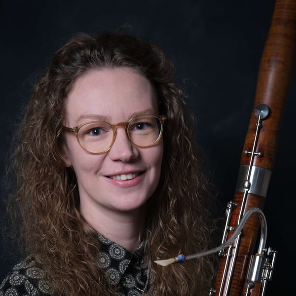 Portrait of Angharad Thomas holding a bassoon, smiling to camera.
