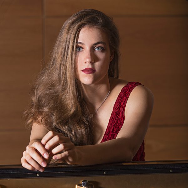 Anna Szałucka looks solemnly to camera while leaning on a piano.