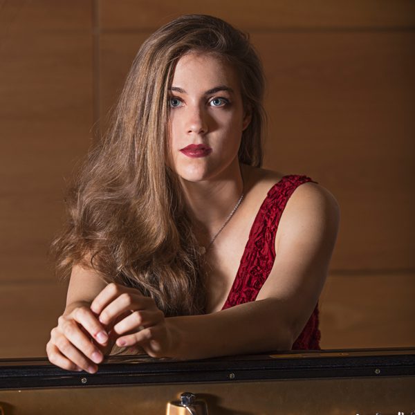 Anna Szałucka looks solemnly to camera while leaning on a piano.