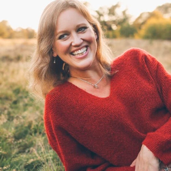 Anna Tilbrook smiles off camera, laying on grass on a sunny day