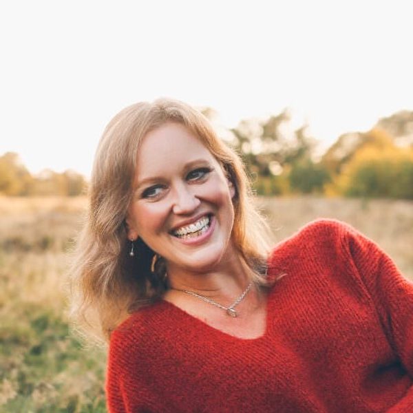 Anna Tilbrook smiles off camera, laying on grass on a sunny day.