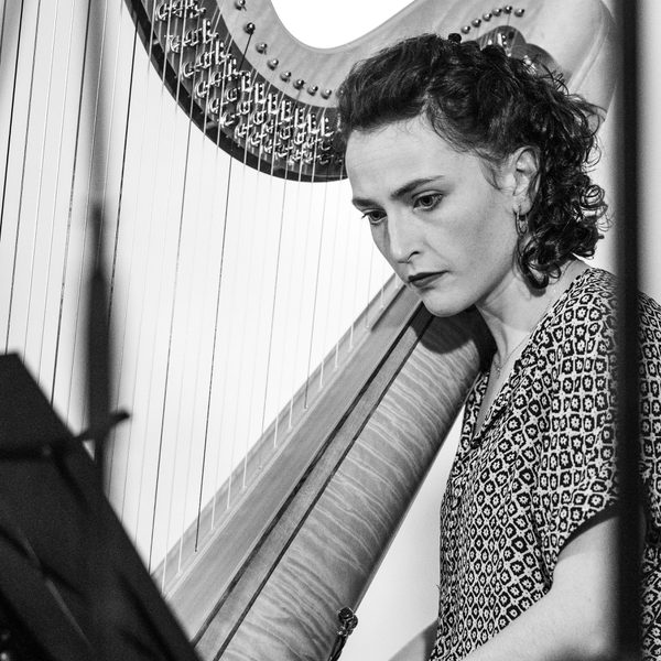 Anne Denholm-Blair sits next to a harp, reading sheet music (black and white).
