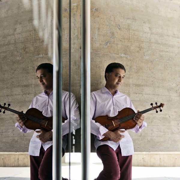Ashan Pillai stands next to a mirror with a violin.